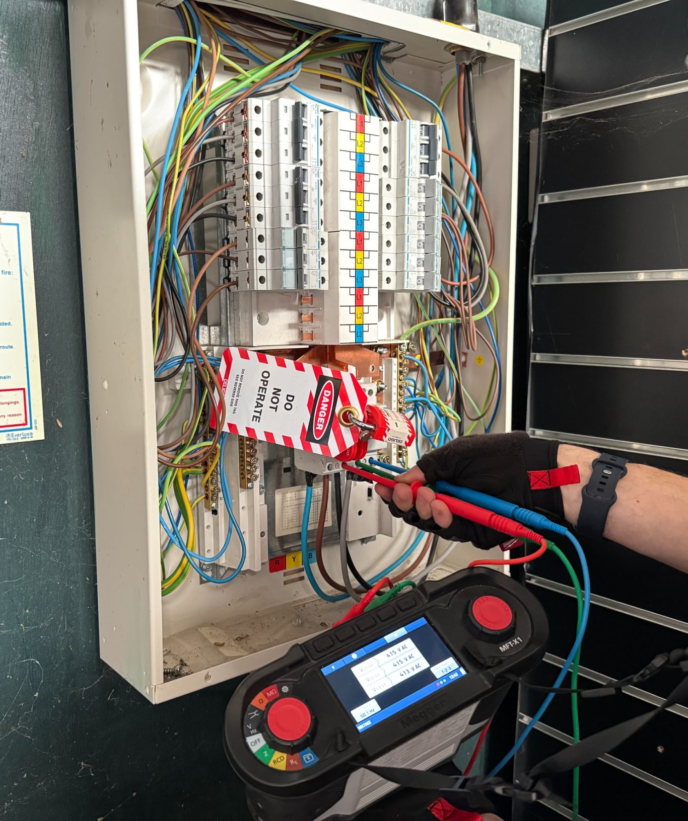 Electrical circuit panel with multicoloured wires and testing equipment in use.